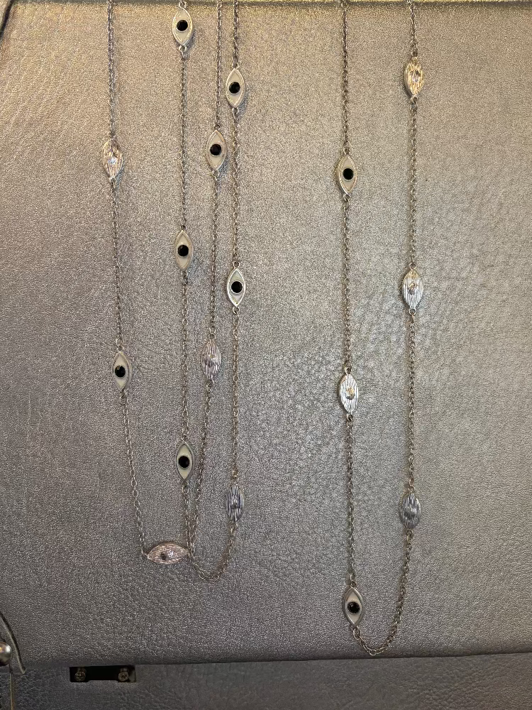Silver chain necklaces with eye-shaped pendants on a gray surface