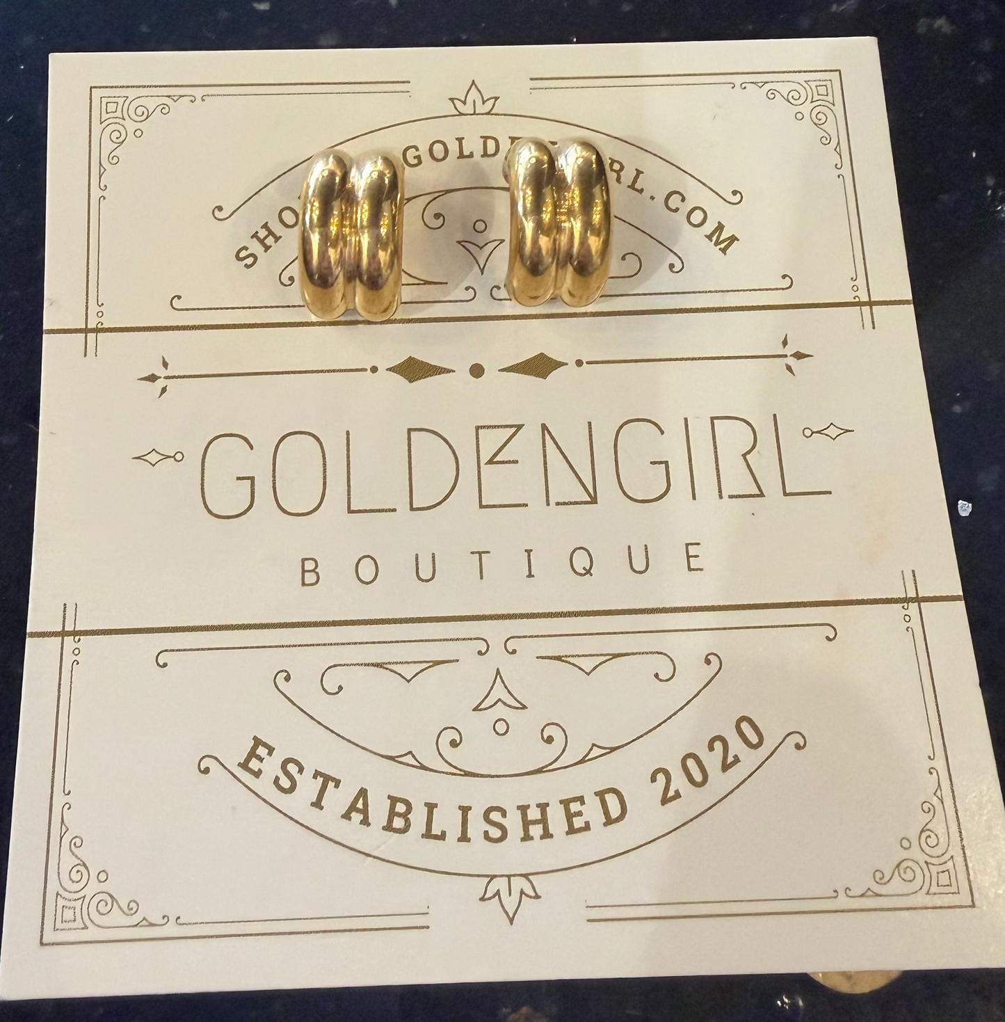 Gold earrings on a card from Goldengirl Boutique with 'Established 2020' text.